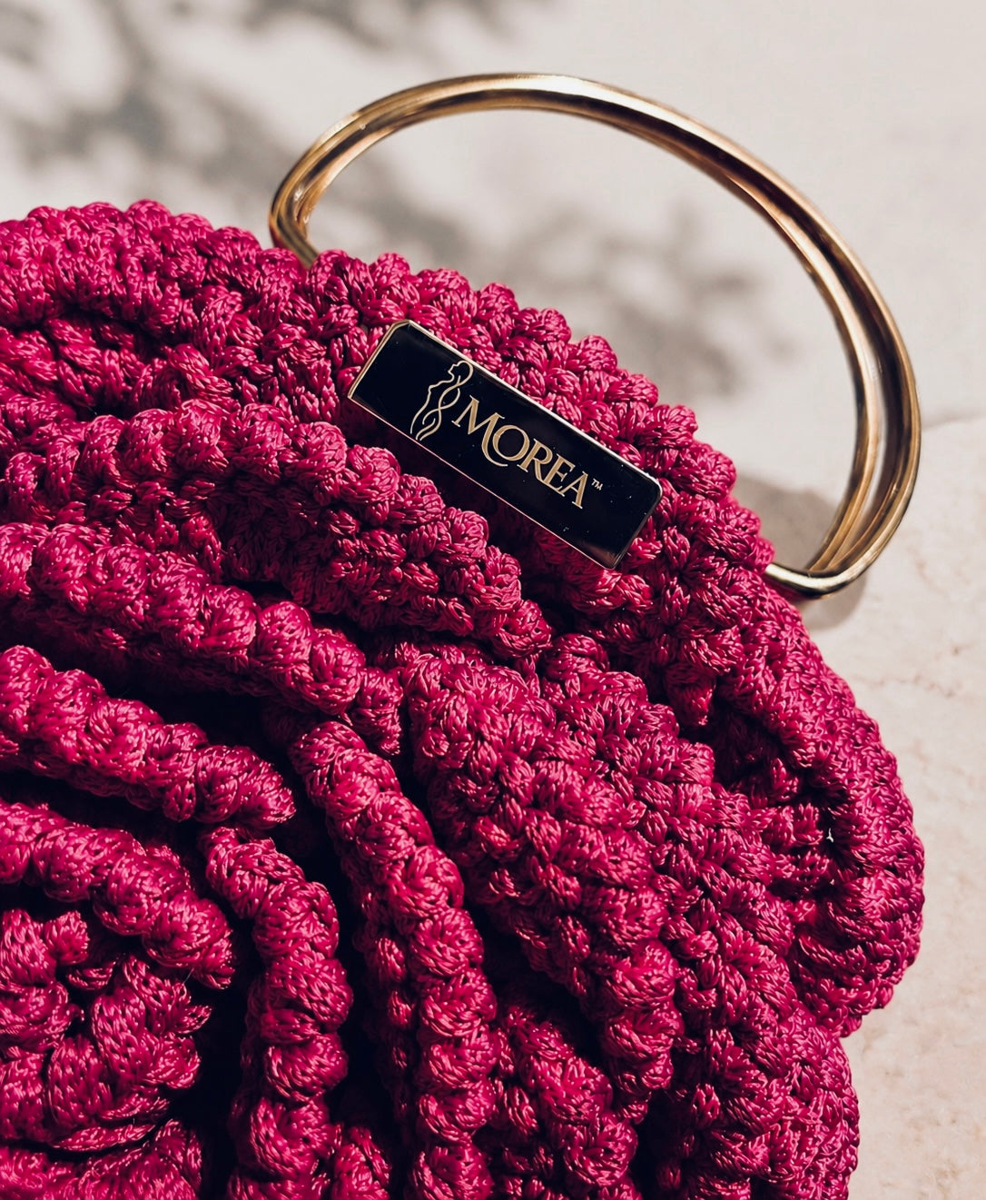 Close-up of the pink crochet rose clutch bag showing the gold handle and MOREA logo tag.